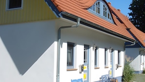 A two-story building with a red-tiled roof, a small porch with a bench, and a window with a blue frame. - 'Haus Windroos' with Private Terrace, Garden, and Wi-Fi (Zingst)