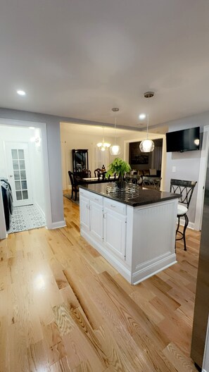A modern kitchen with a central island, wooden flooring, white cabinetry, and pendant lighting. - Spacious 3BR Home - Sleeps 10 - Perfect for Families & Groups. (Utica)