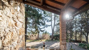 A stone wall with a metal table and chairs, a bottle of wine, and a view of trees and a body of water.