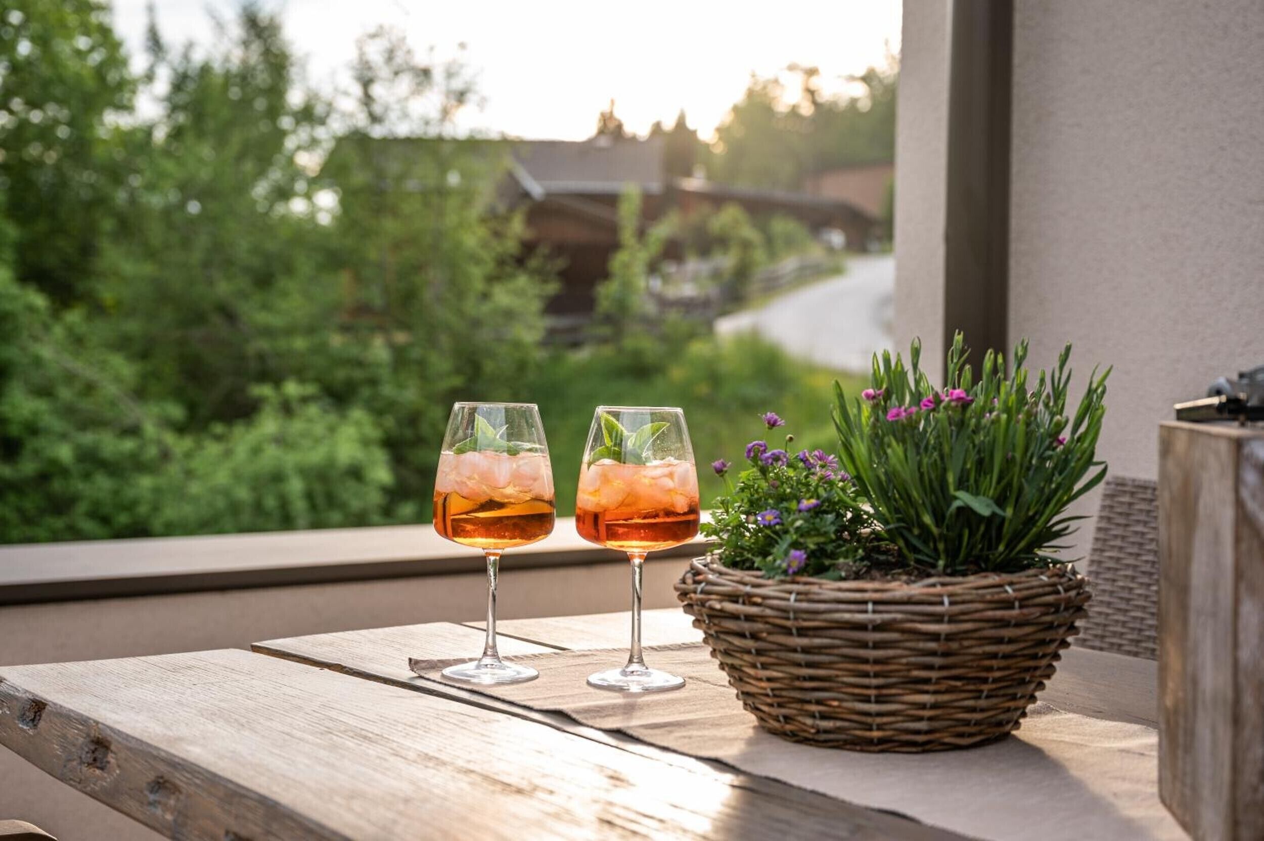 Two glasses of a beverage on a wooden table with a wicker basket containing a plant.