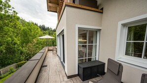 Ein moderner Balkon im Freien mit einer Bank, einem Liegestuhl und einem Tisch.