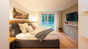 Ein Schlafzimmer mit einem Bett, einem Fernseher, einem Fenster mit Vorhängen und einem Bild an der Wand.