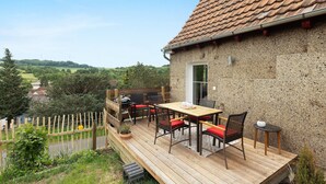 Eine Holzterrasse mit Gartenmöbeln, einem Grill und Blick ins Grüne.