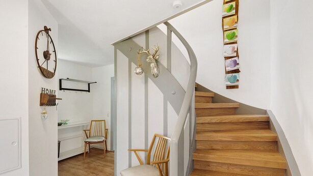 Eine Treppe mit Holzboden und Metallgeländer, ein Holzstuhl, ein Schreibtisch mit Stuhl und eine Wanduhr.