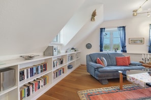 A cozy living room with a blue sofa, a bookshelf filled with books, and a wooden floor.