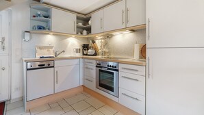 Una cocina con armarios blancos, lavavajillas, horno y encimera con varios electrodomésticos.