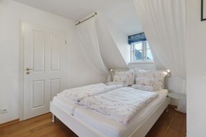 Ein Schlafzimmer mit Bett, Vorhängen, Fenster und Tür.