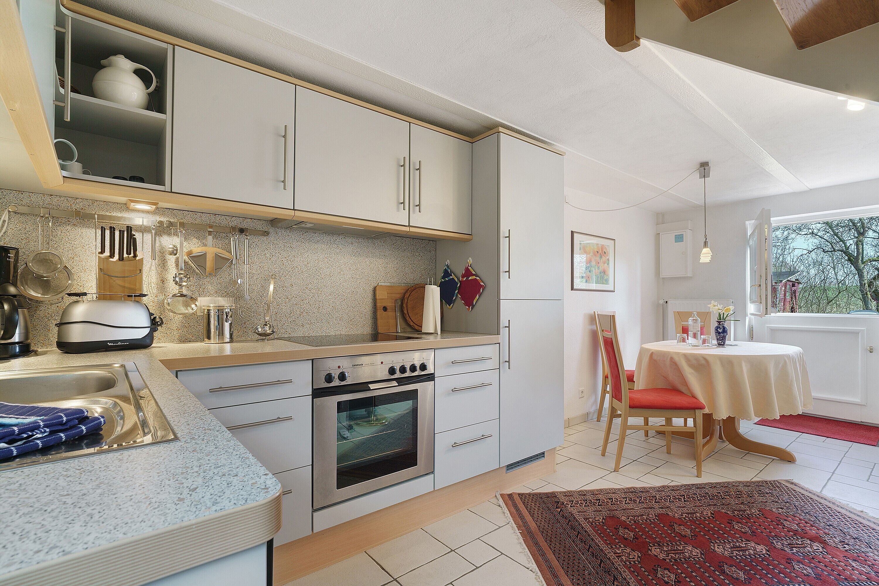 Una cocina con estufa, horno y lavabo, una zona de comedor con mesa y sillas, y un ventanal con vistas.