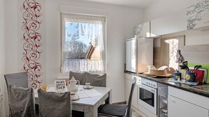Cocina compacta con mesa, sillas, refrigerador y ventana con cortinas.