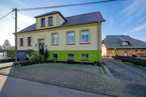 A two-story building with a green and yellow facade, a tiled roof, and a paved driveway. - Apartment 'Familienfreundliche' with Private Garden and Wi-Fi (Kenz-Küstrow)