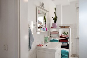 A bathroom with a white sink, mirror, shelves with towels, and potted plants. - Apartment 'Familienfreundliche' with Private Garden and Wi-Fi (Kenz-Küstrow)