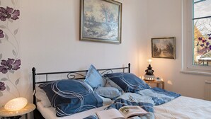 Un dormitorio con cama, almohadas, una mesita de noche con lámpara, y dos cuadros en la pared.