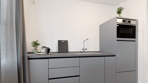 Een moderne keuken met grijze kastjes, een inbouwoven, een koffiezetapparaat en een kleine potplant.