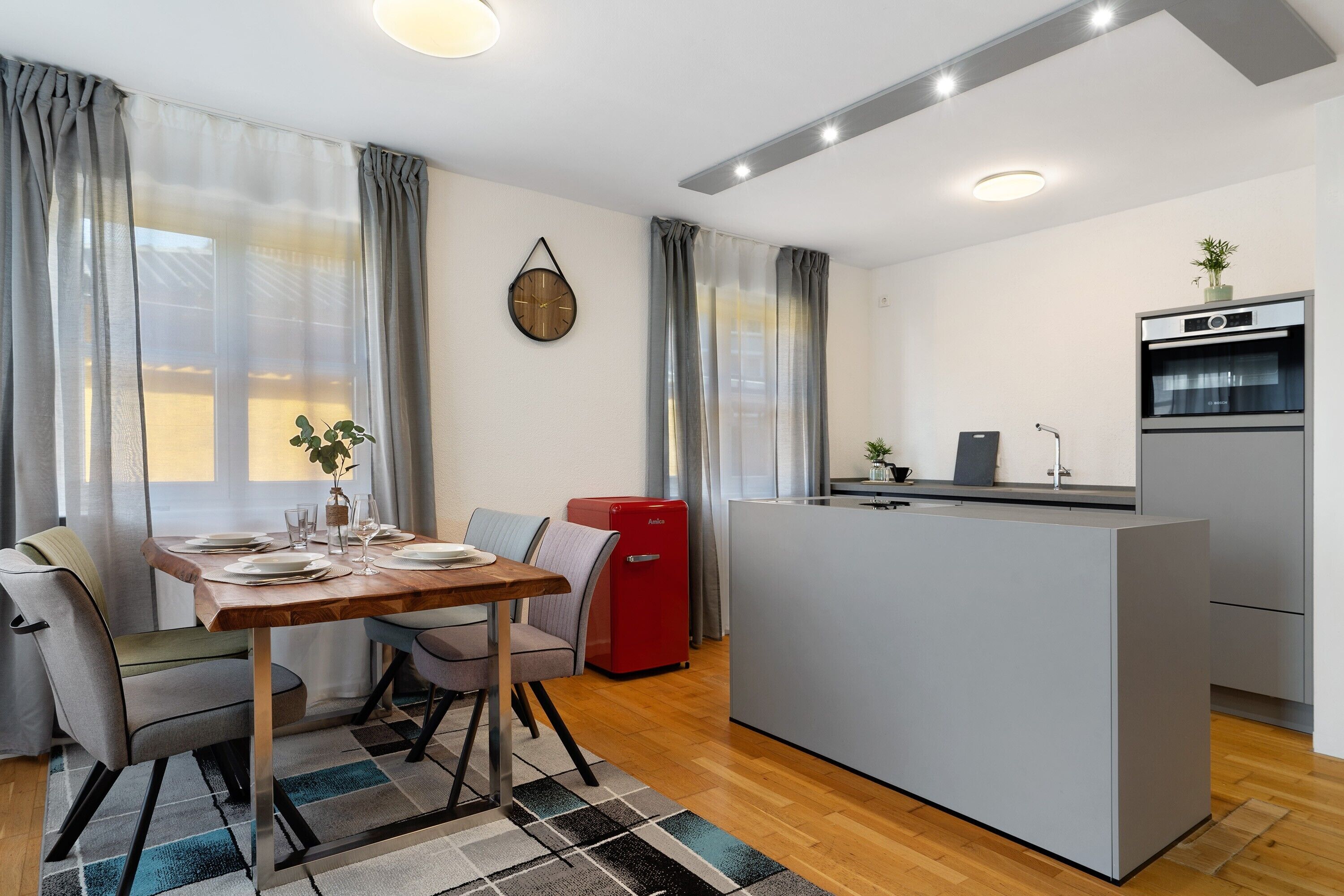 A compact kitchen with a central island, a dining area with a table and chairs, and a red appliance.