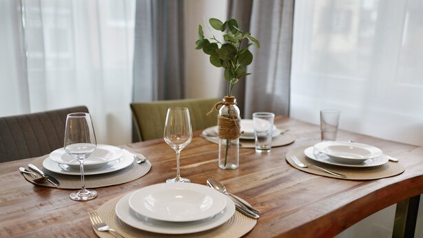 Een houten eettafel gedekt met borden, bestek en een glazen vaas met een plant.