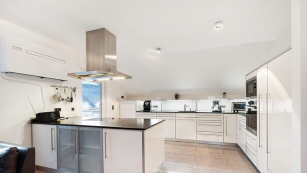 A modern kitchen with white cabinetry, a central island, stainless steel appliances, and a hanging pot rack.