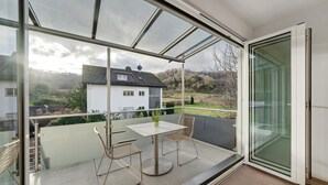 A modern room with a glass door leading to an outdoor balcony, a small table with chairs, and a potted plant.