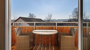 En udendørs balkon med et rundt bord og to fletstole, gelænder af træ og udsigt over landskabet.