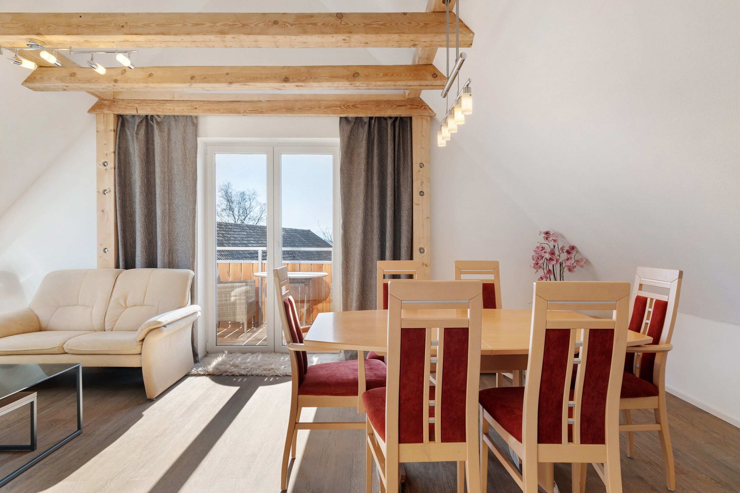 Ein modernes Wohnzimmer mit einer Couch, einem Esstisch, Stühlen und Blick durch ein großes Fenster.