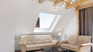 En moderne stue med højt til loftet, et ovenlysvindue, to beige sofaer, et sofabord i glas og en lampe.