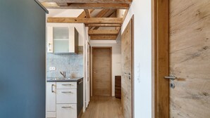 En smal gang med en trædør, et tekøkken med skabe og en vask, samt et flisebeklædt backsplash.