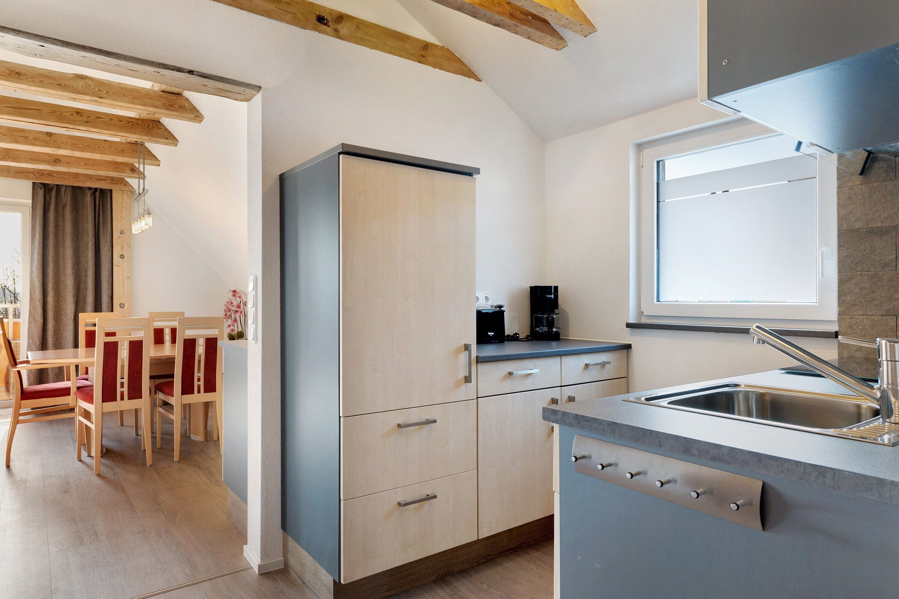 Une cuisine moderne équipée d’un réfrigérateur encastré, d’un évier et d’un coin repas avec des chaises et une table en bois.