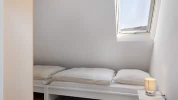 A small, white, single-bed room with a skylight and a bedside lamp.
