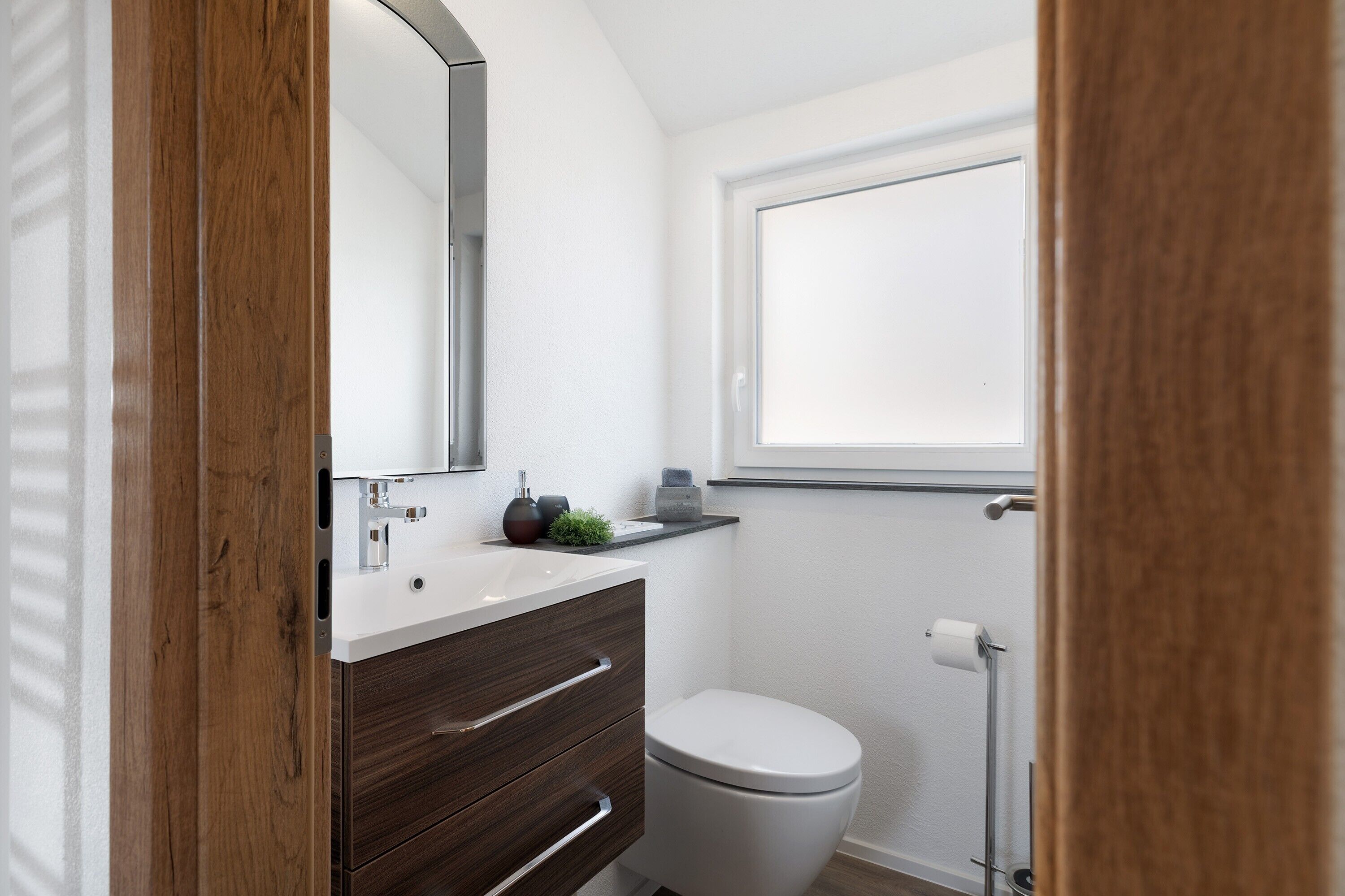 A bathroom with a white toilet, a wooden vanity with a mirror, and a small shelf with toiletries.
