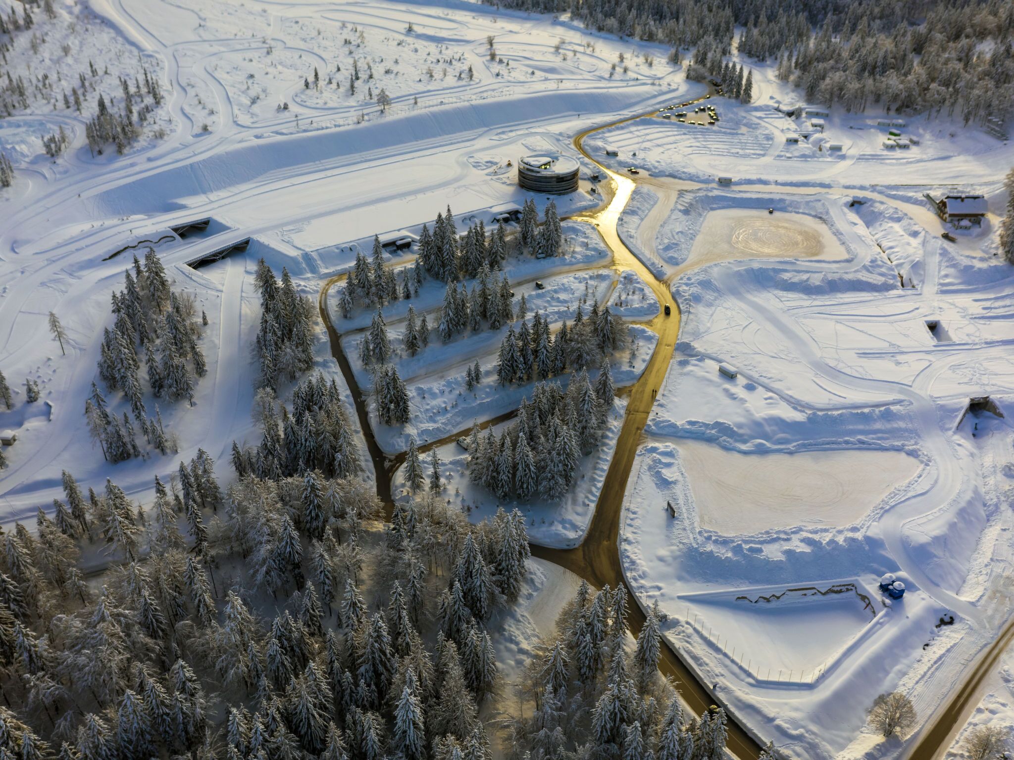 Une vue aérienne d’un paysage enneigé, avec une route sinueuse, des bâtiments et une rivière.