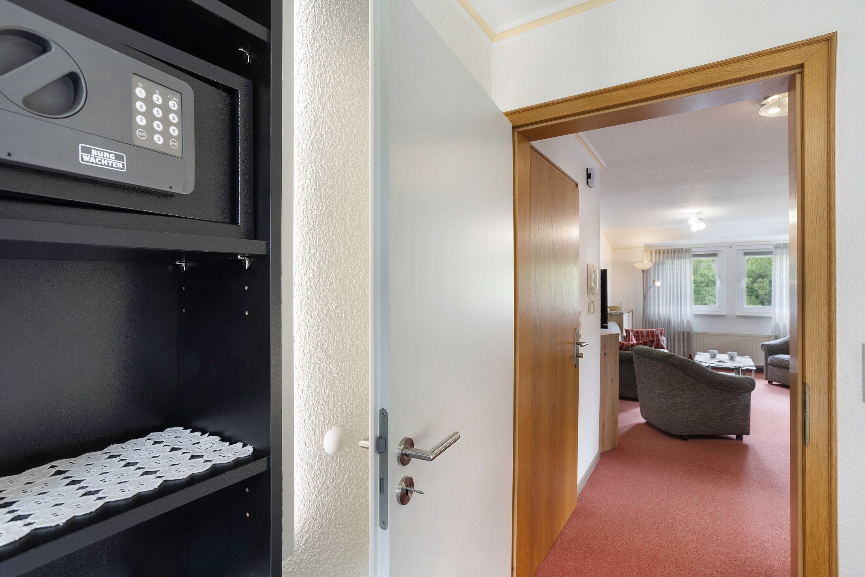 A hotel room with a door leading to a living area, a minibar, and a control panel.