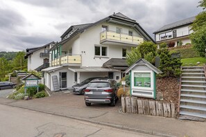 Un immeuble de deux étages avec un balcon, une voiture garée devant et une enseigne.