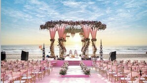 En bröllopslokal på stranden med en scen, stolar och blomsterdekorationer.