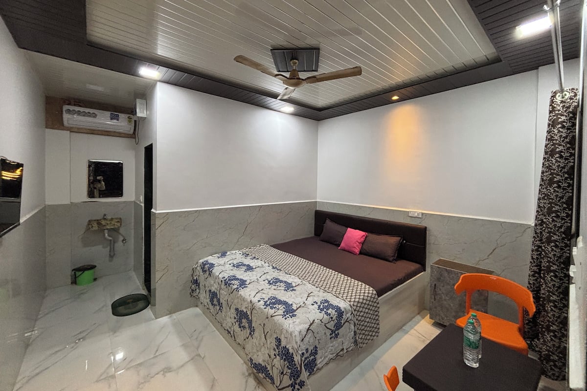 A modern bedroom with a bed, a ceiling fan, a small table with a bottle, and a chair.