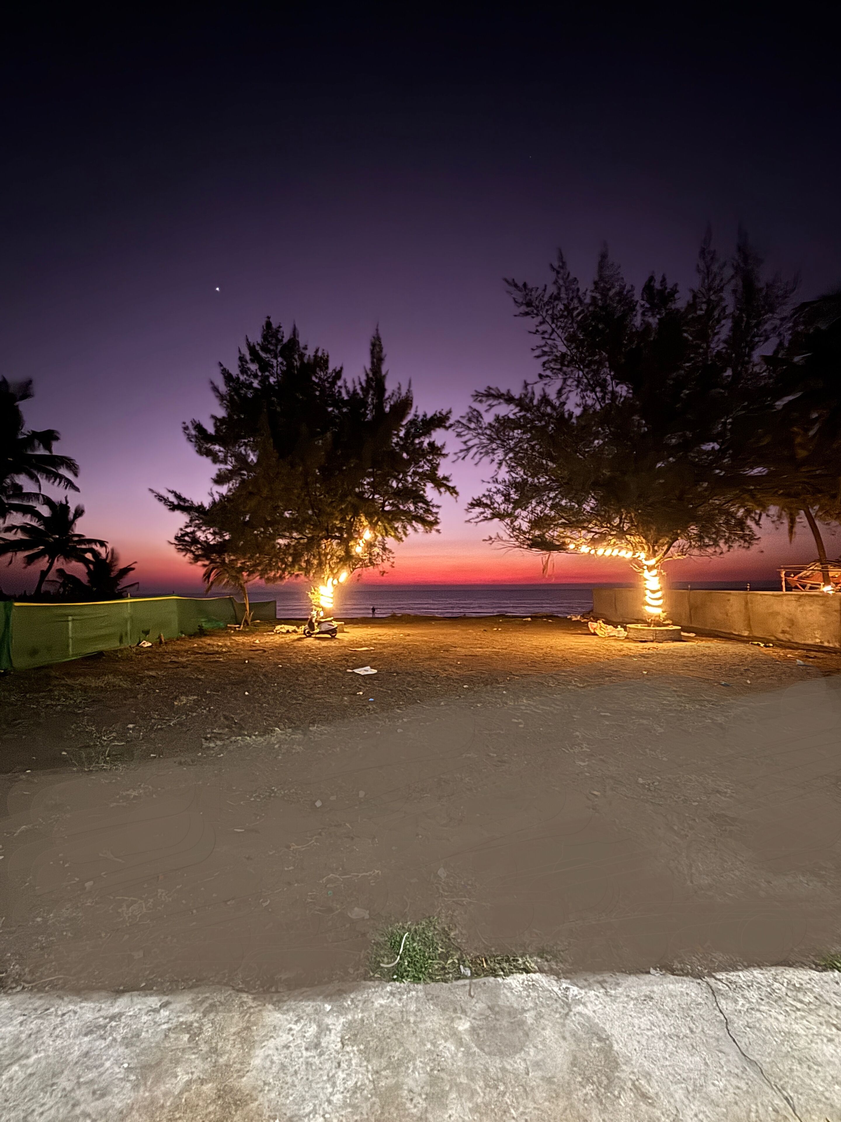 Une scène de plage nocturne avec un coucher de soleil, des arbres et une clôture.