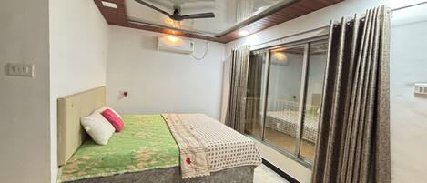 Un dormitorio con cama, ventilador de techo, aire acondicionado y vistas por una puerta corrediza de vidrio.