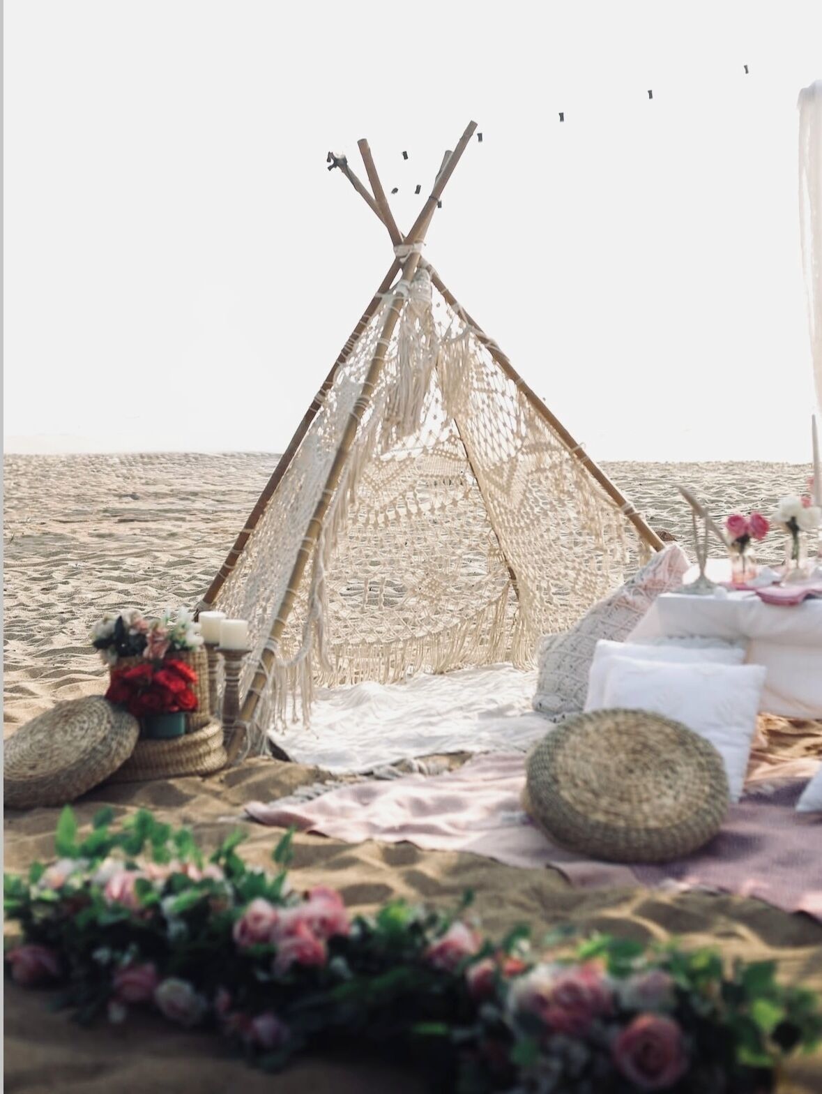 A beach setting with a woven tent, a table with white linens, and floral decorations.