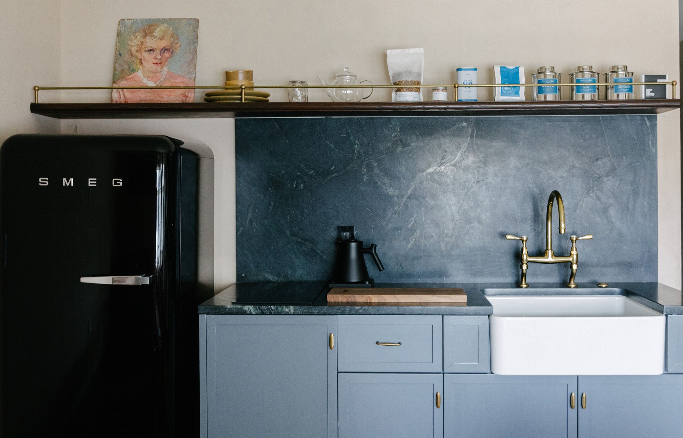 Una cocina con un refrigerador negro, una cafetera y un lavamanos con grifo de latón.