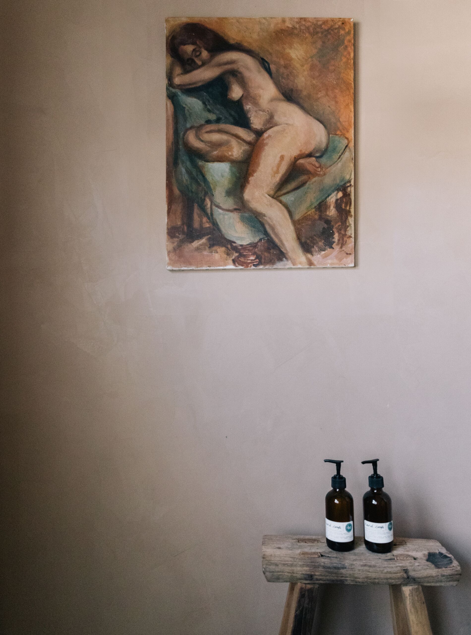 A painting of a reclining figure on a chair, two bottles on a wooden stool below.