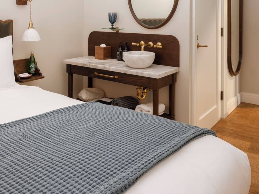 Une chambre d’hôtel comprenant un lit, une table de chevet avec une lampe, un miroir, une salle de bain avec un lavabo et une porte.