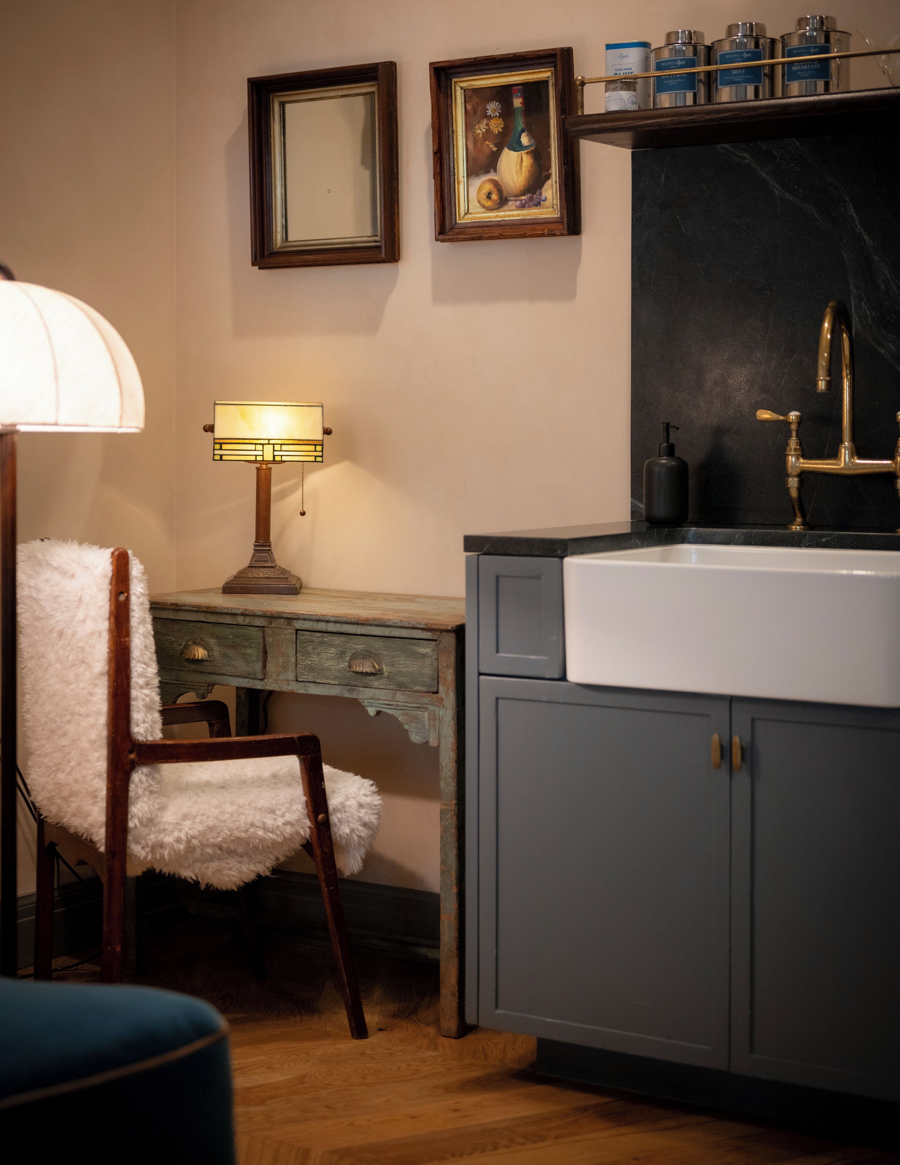A kitchen with a sink, a chair with a white towel, a lamp, and a shelf with containers.