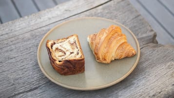 A wooden bench with a plate containing a slice of bread and a croissant.
