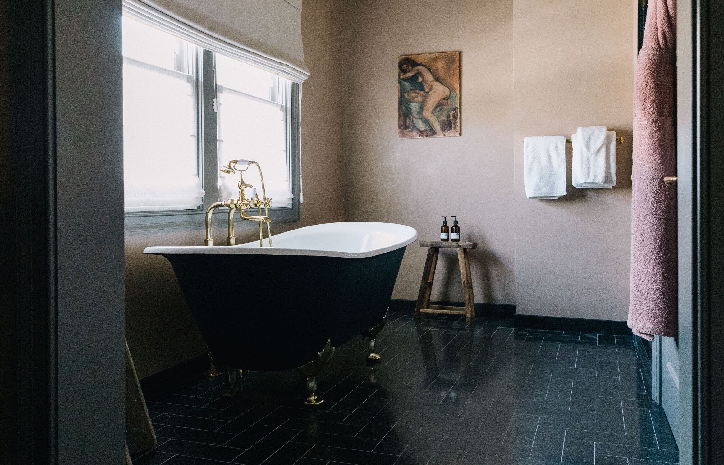 Ein Badezimmer mit freistehender Badewanne, einem Fenster, einem Bild an der Wand und Handtüchern auf einem Wäscheständer.