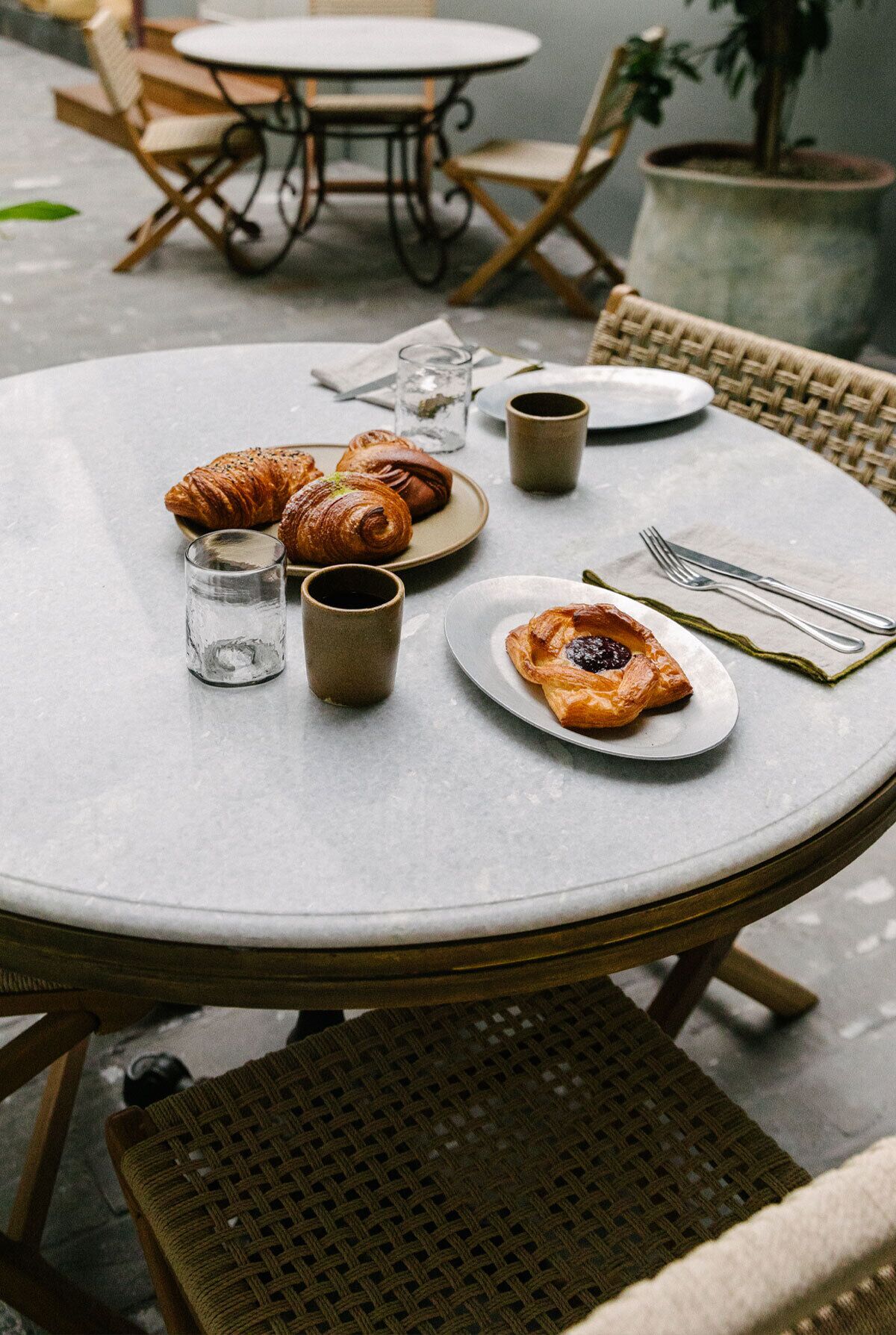 Ein runder Esstisch mit einer Platte Croissants, einem Glas Wasser und einer Tasse.