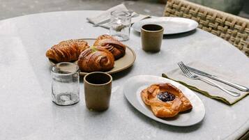 Ein runder Esstisch mit einer Platte Croissants, einem Glas Wasser und einer Tasse.