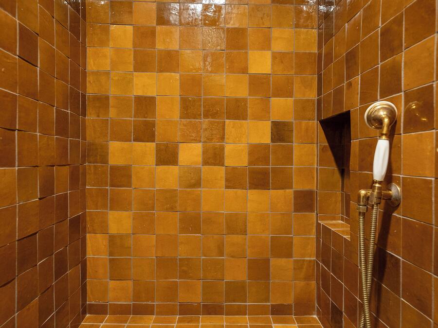 A shower with brown tiles and a handheld showerhead.