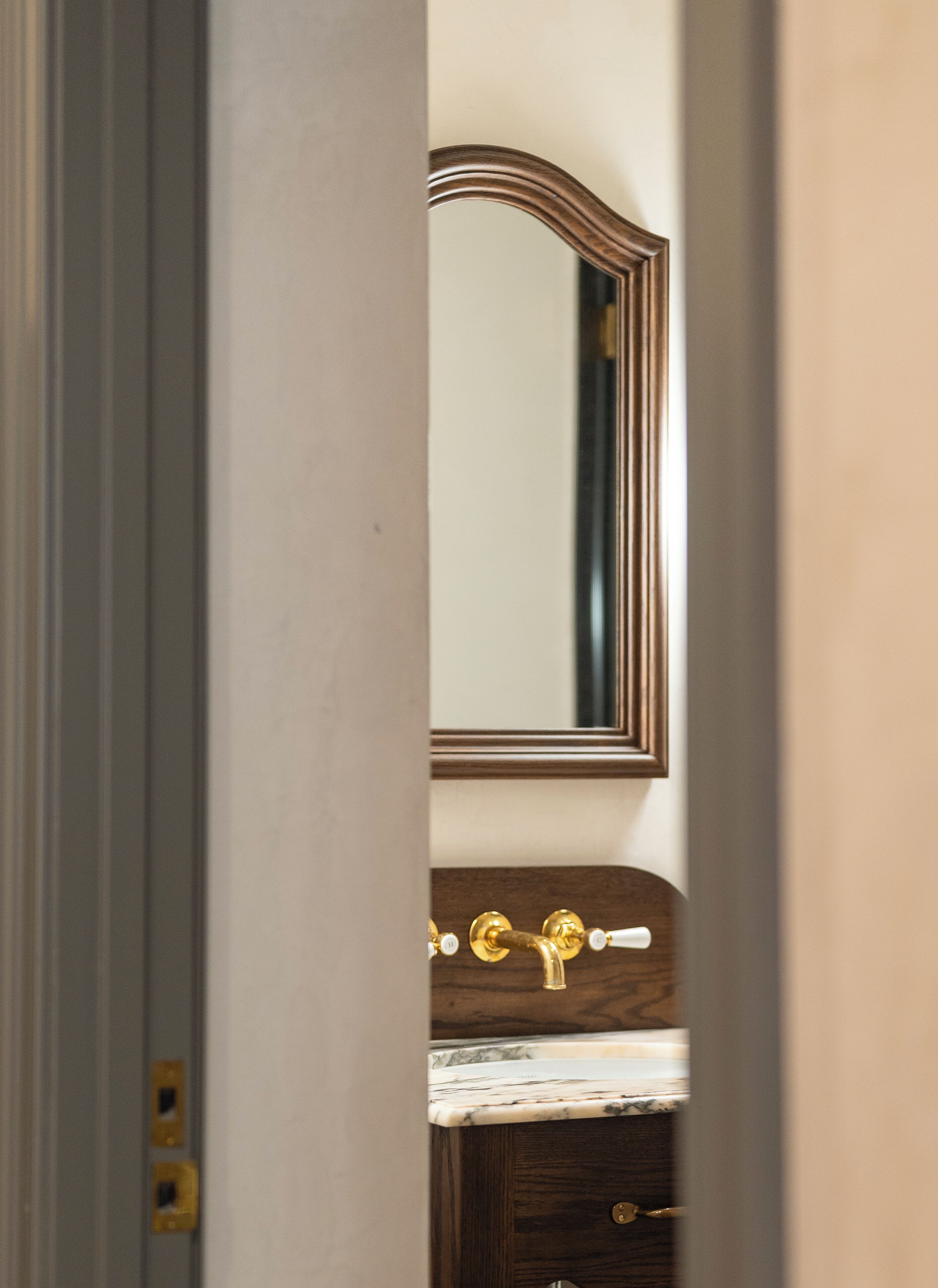 A bathroom with a wooden vanity, a marble countertop, and a gold faucet.