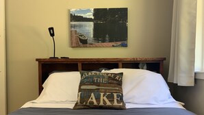 Una camera da letto con un letto, un cuscino con motivo a tema lago, una testiera in legno e un quadro raffigurante una scena lacustre sopra il letto.