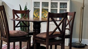 Zona pranzo con tavolo e sedie, una lampada, un mobile con ante in vetro e un quadro appeso al muro.