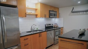 Una cucina moderna con elettrodomestici in acciaio inossidabile, mobili in legno e un piano di lavoro nero.