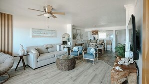 A spacious living room with a ceiling fan, a sofa, armchairs, a coffee table, and a dining area with a table and chairs.